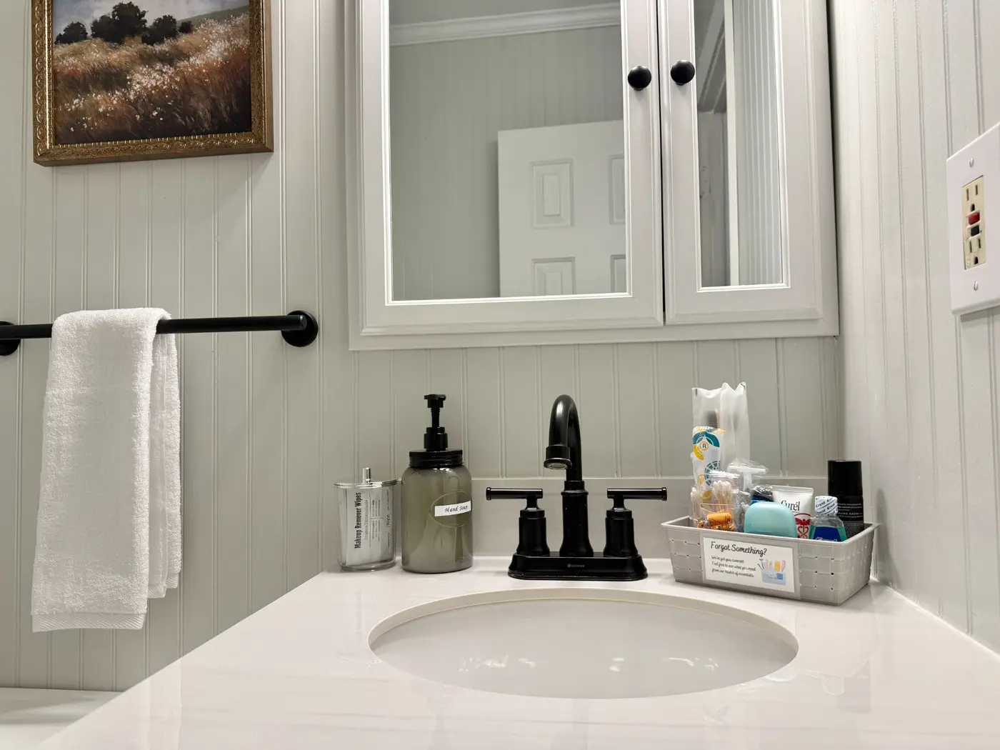 Bright bathroom vanity with a fresh white towel, labeled hand soap, and a thoughtfully stocked basket of guest essentials