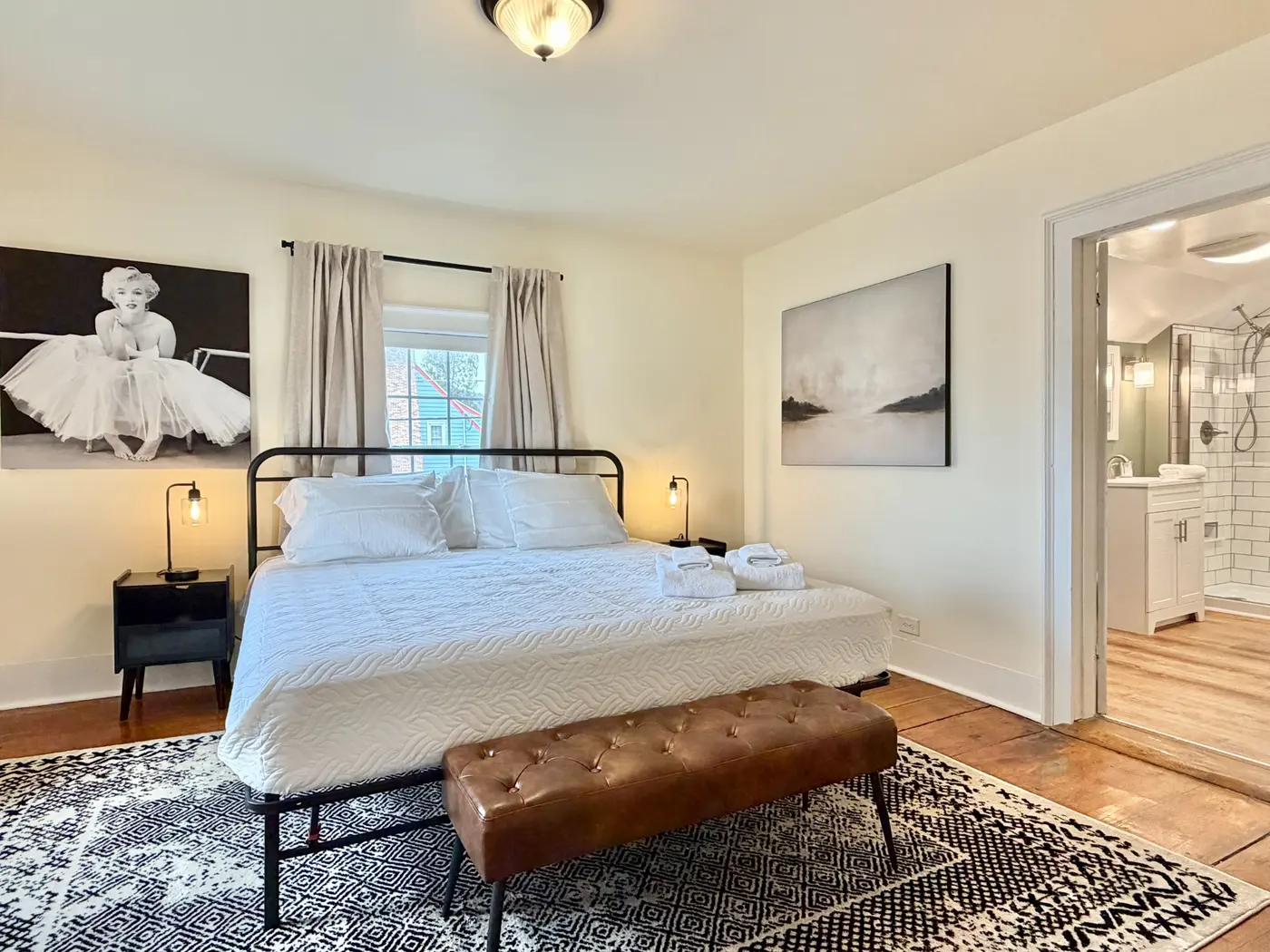 Bright, professionally prepared guest bedroom with crisp white bedding, folded towels, and an adjoining tiled bathroom